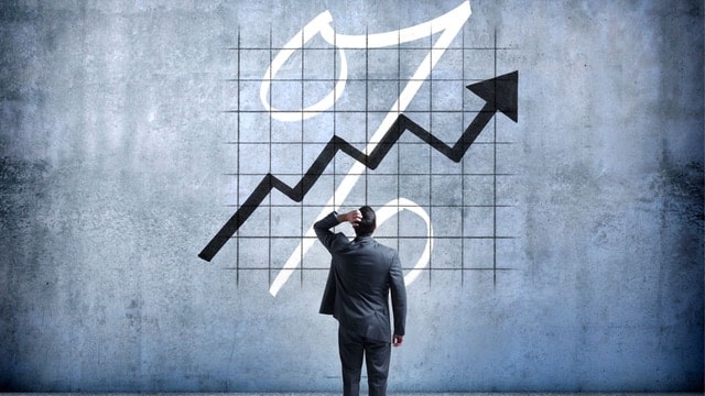 Businessman analyzing an upward trend graph symbolizing the process of calculating cap rates in real estate against a grid backdrop