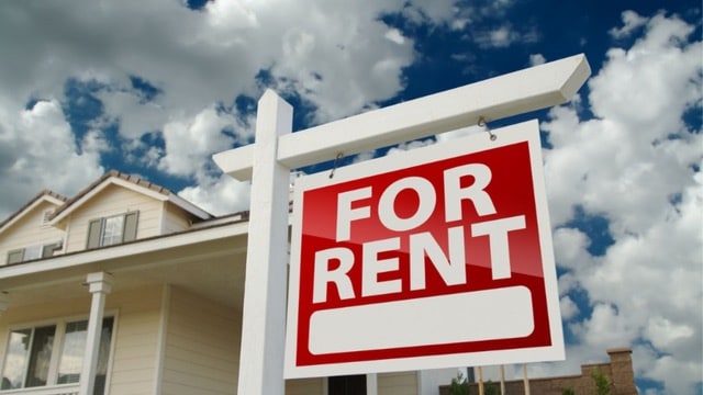 Red 'For Rent' sign in front of a house, symbolizing April 2024 rental market trends in real estate