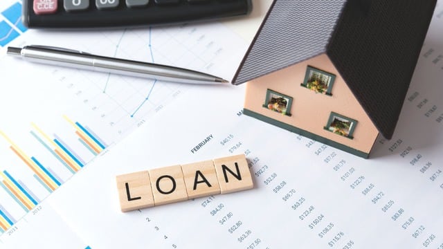 Small model house next to 'LOAN' spelled in wooden letters, on top of financial charts, symbolizing the Private Lending Checklist