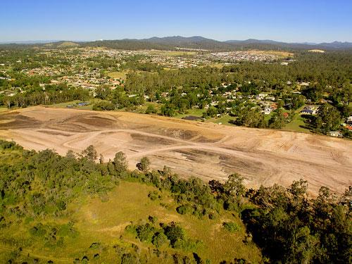 Aerial view of a land development site with partially cleared land and surrounding forested and residential areas, showcasing the transition from undeveloped land to potential residential or commercial use.