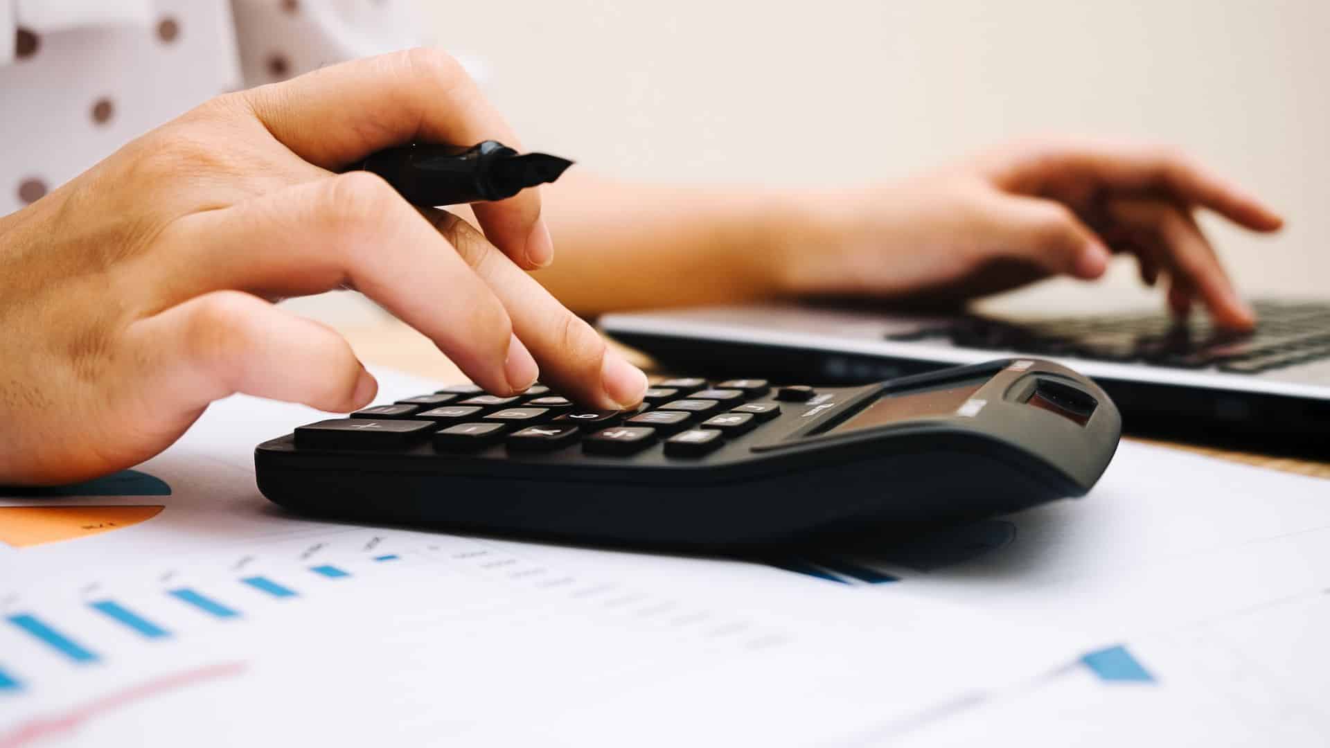 A person using a calculator and pen to calculate financial figures, representing the process of determining Net Operating Income (NOI) for real estate investments.